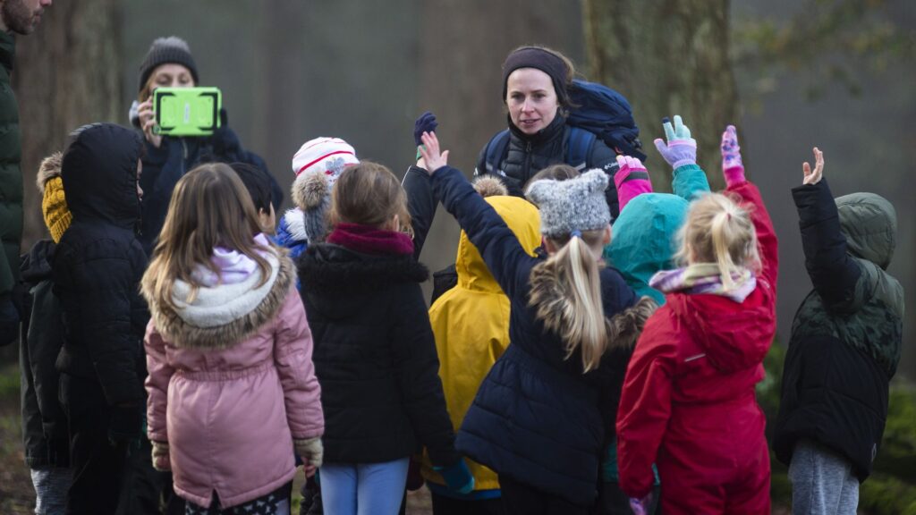 A group of young children with their arms in the air in front of a woman with a headband