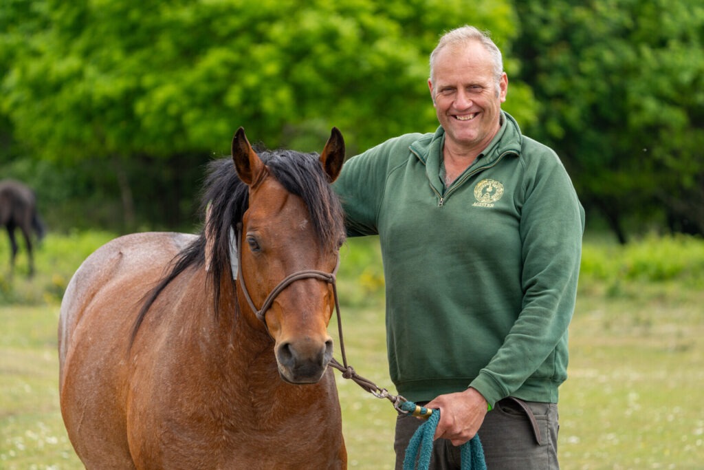 A man in a green top smiling alongside a pony