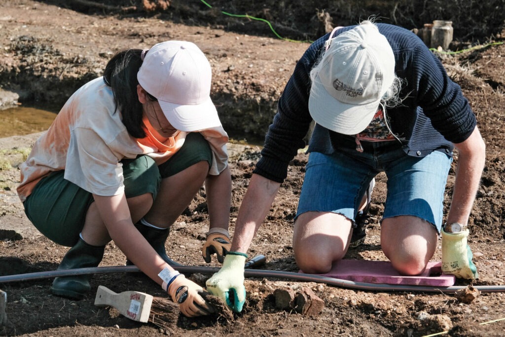 Two people in caps on their knees looking at objects in the ground