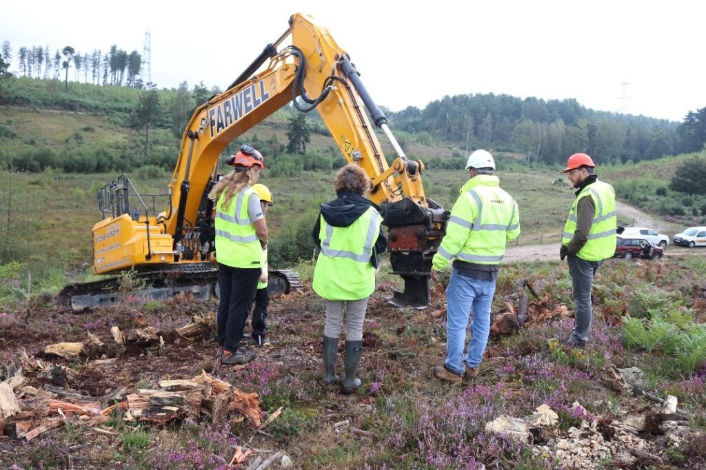 Four people in high vis jackets standing around a digger