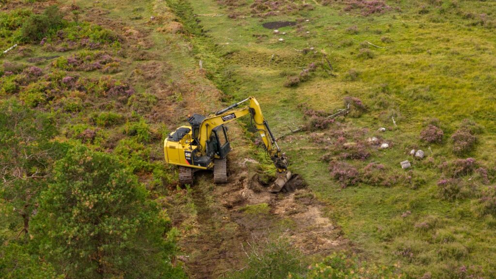Excavator digging a trench in a grassy moorland during seepage mire restoration work